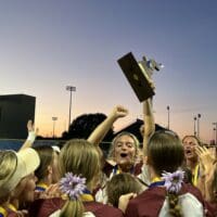Caravel softball pitcher Kasey Xenidis holds up the DIAA state championship trophy with her teammates after defeating Sussex Central. Photo by Shannon Timmons